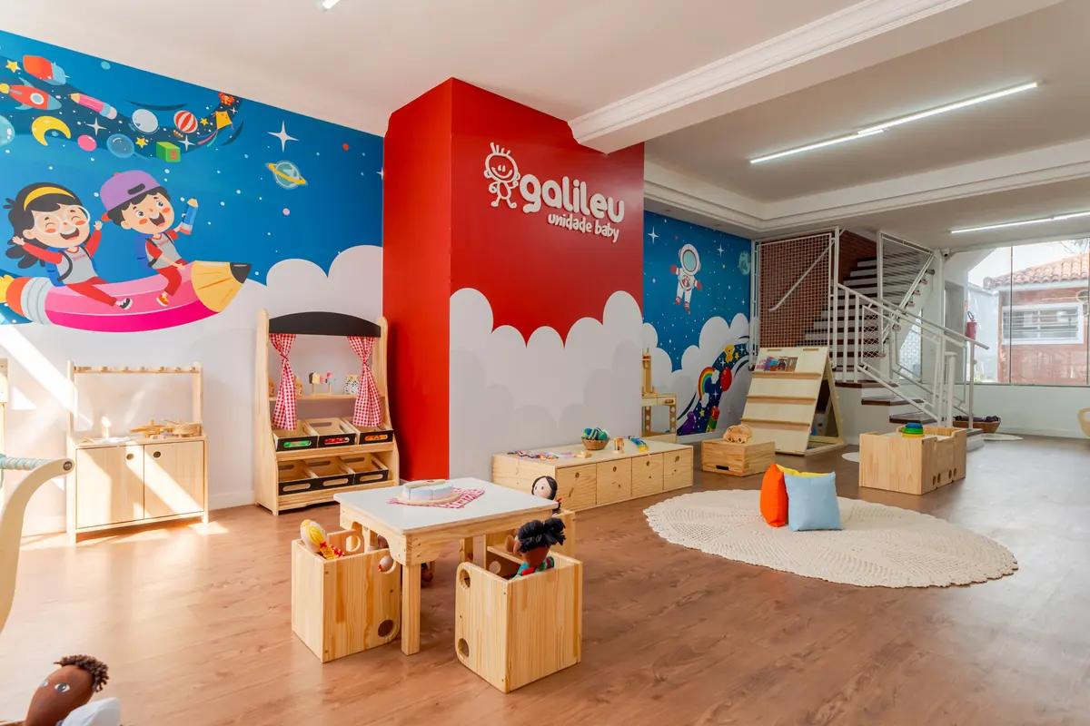 Sala de atividades ampla e iluminada, com mobiliário de madeira e mural colorido