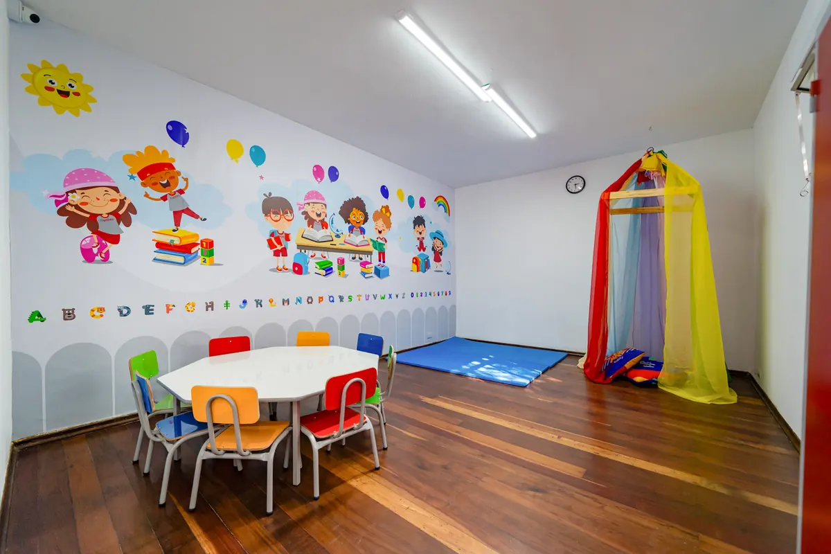 Sala de aula com mesa e cadeirinhas coloridas