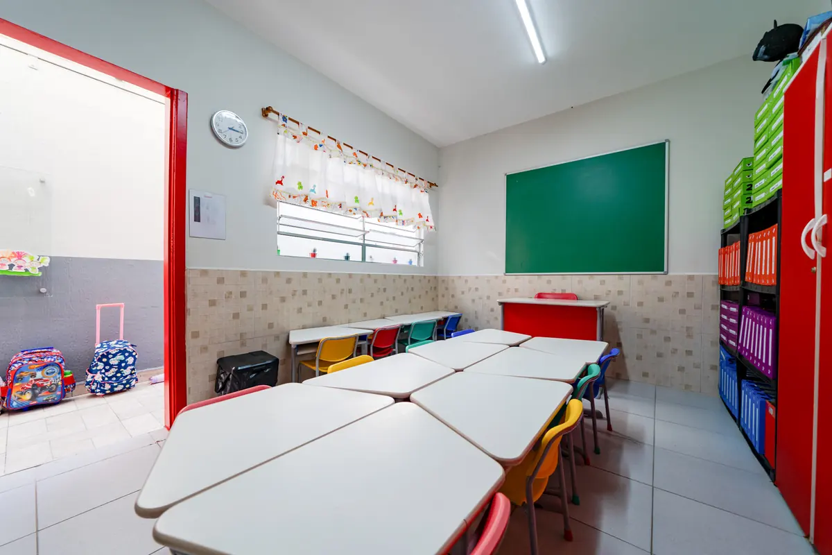 Sala de aula com mesas em grupo, lousa verde e armário vermelho